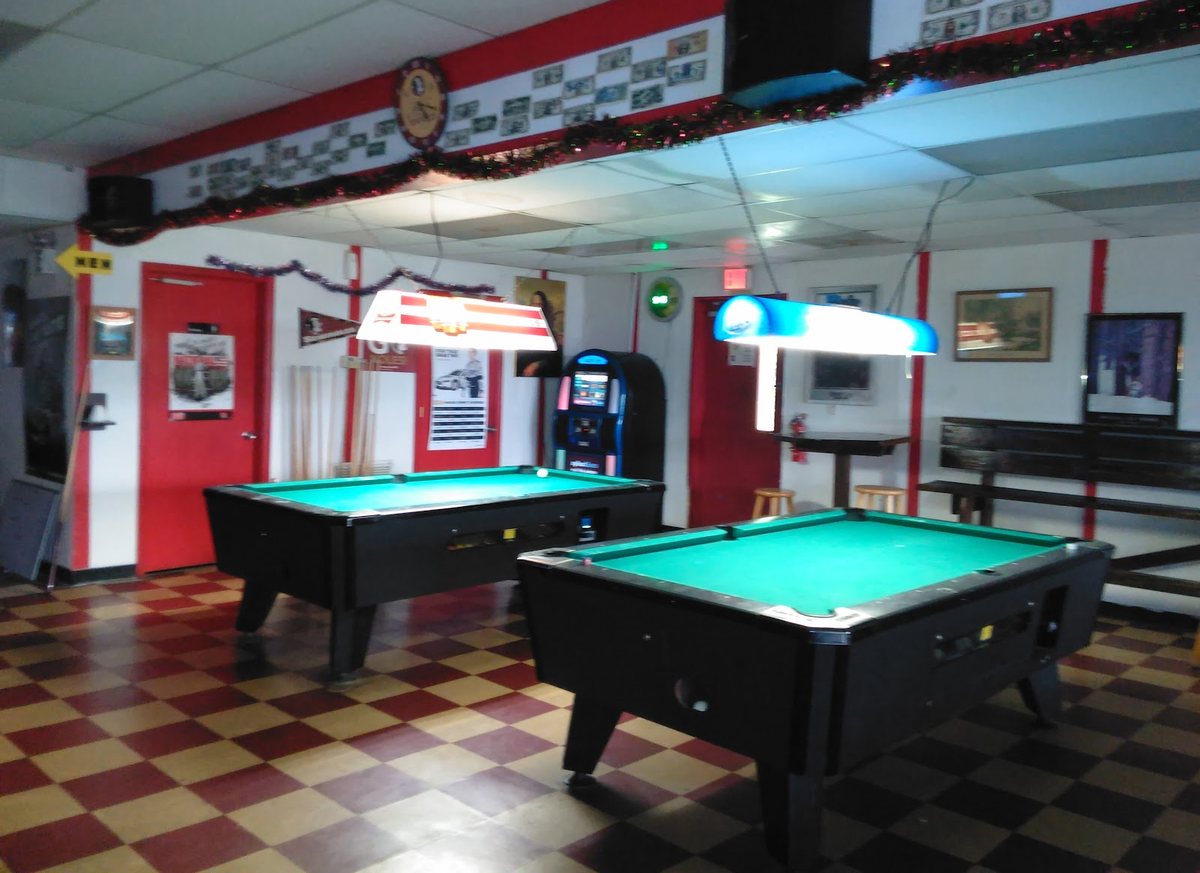 Two pool tables with green felt under hanging lamps, standing on a red and cream checkerboard floor.
