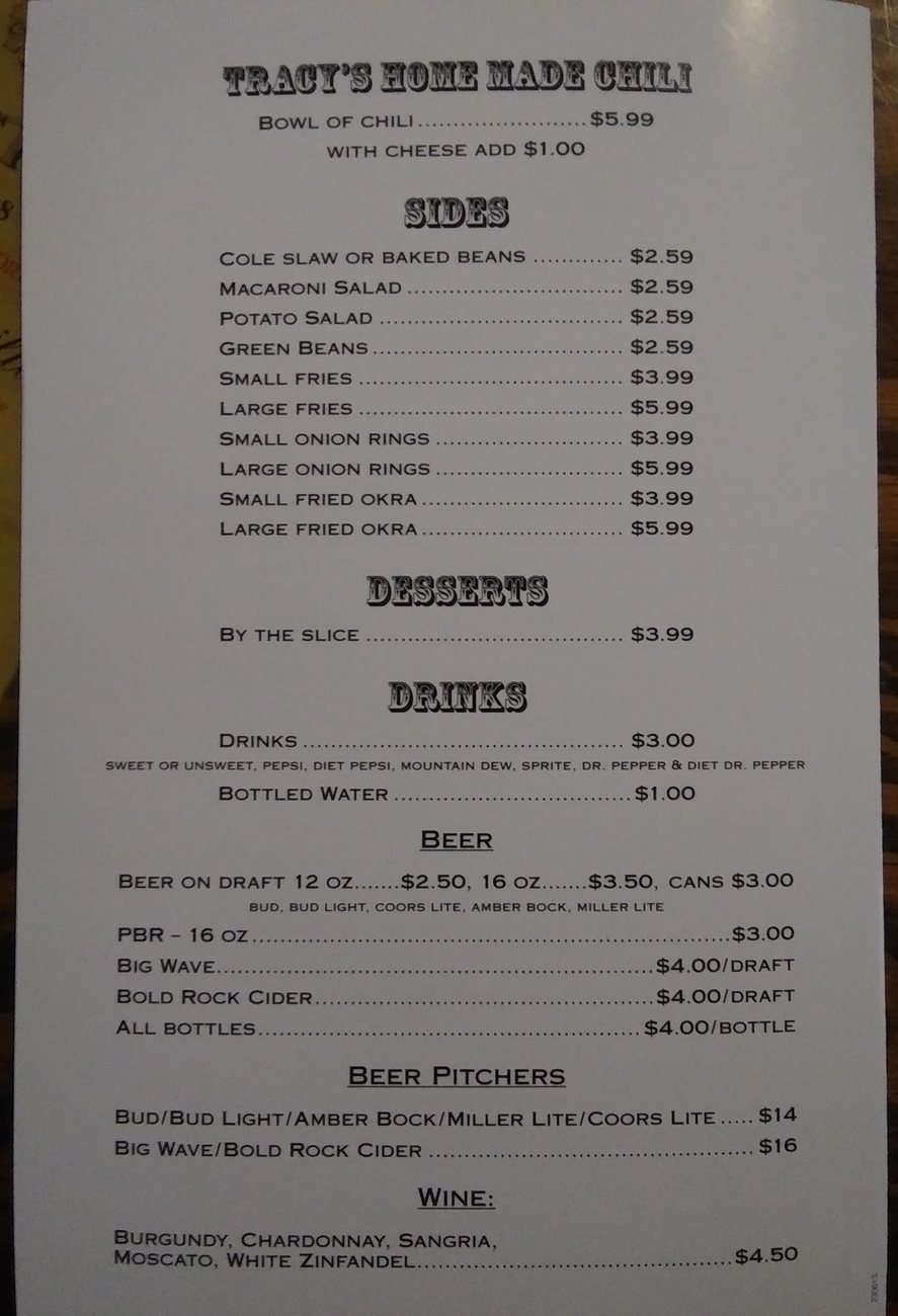 The printed menu on a wooden table, listing chili, sides, desserts, drinks, beer and wine with their prices.