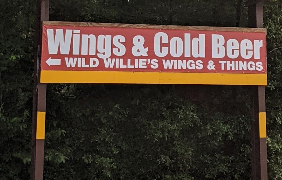 A red roadside banner reading Wings & Cold Beer, Wild Willie’s Wings & Things, with an arrow pointing left.